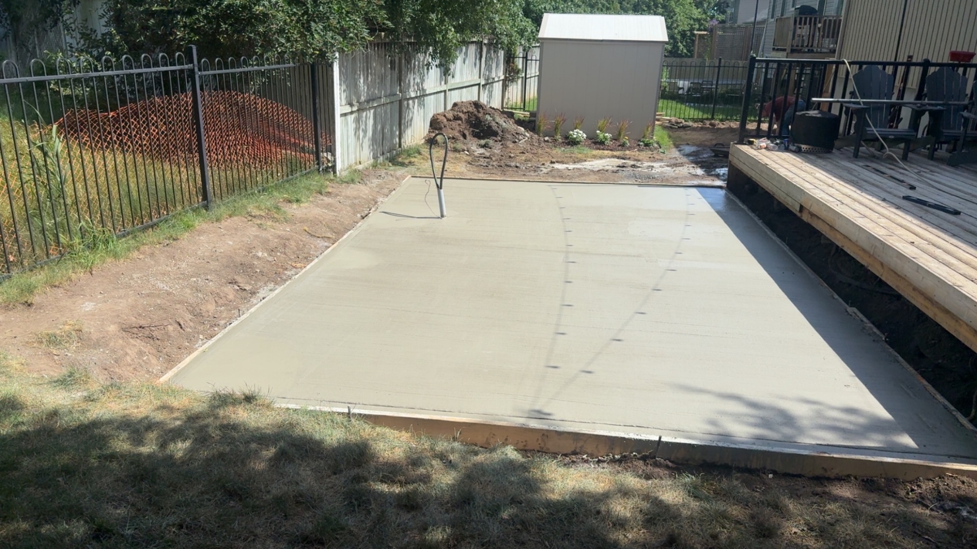 Fresh concrete patio pad poured beside a wooden deck after excavation and grading