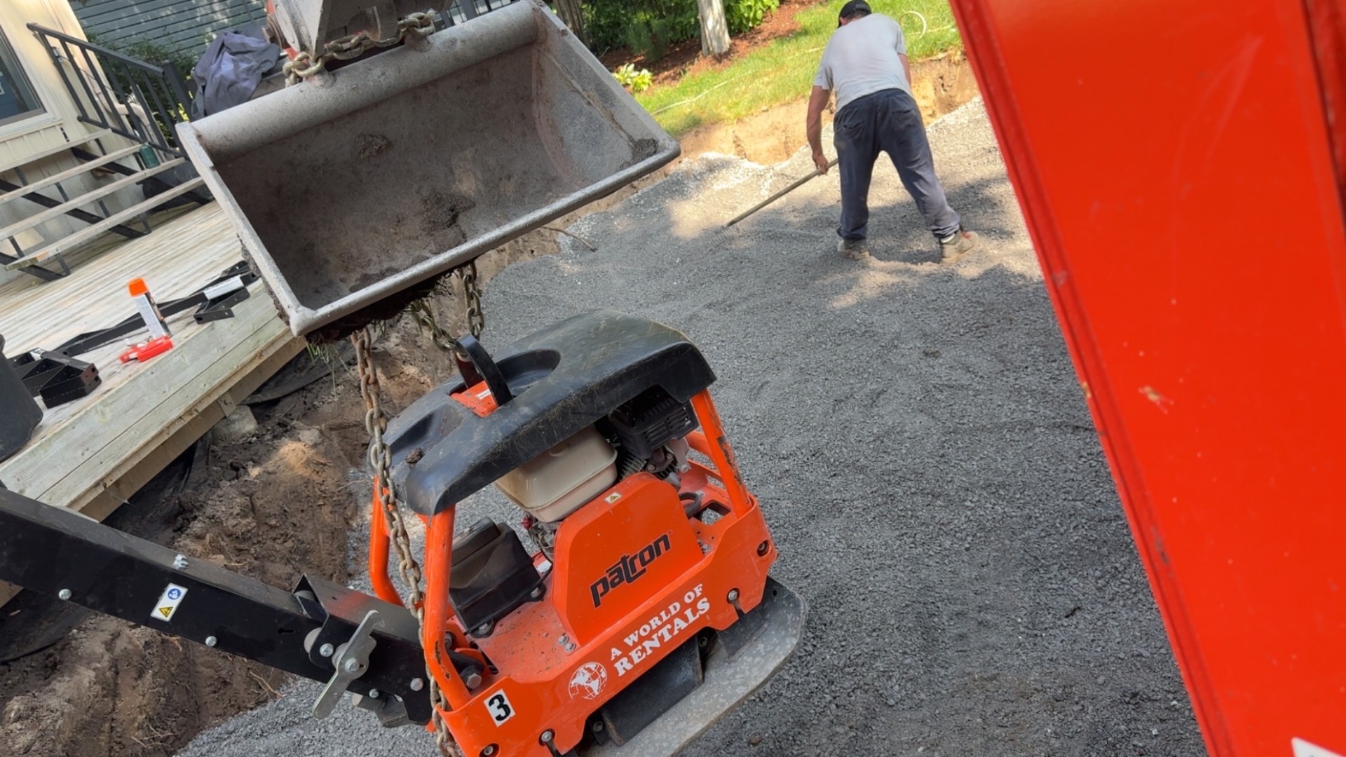 Plate compactor and gravel being spread on a new driveway build