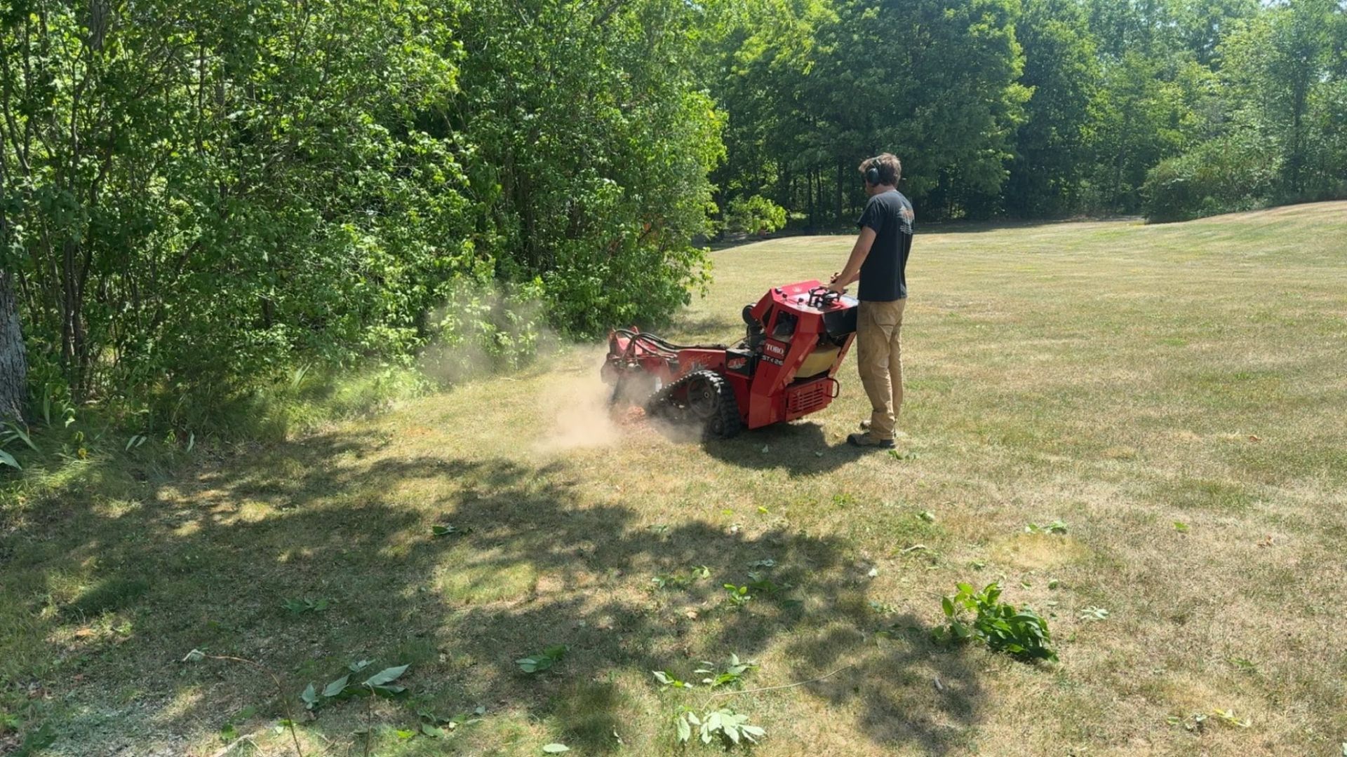 Operator running a stand-on brush cutter along a treeline