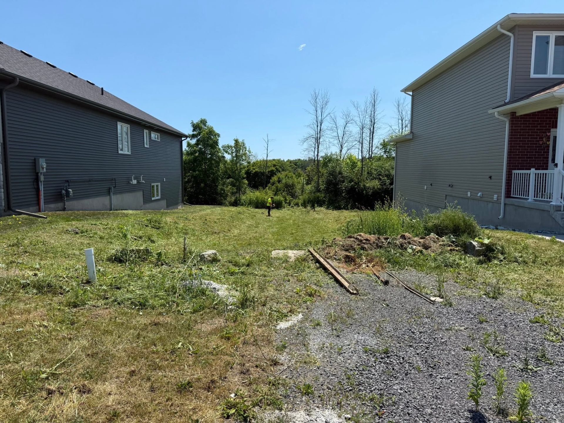 Worker string-trimming an overgrown residential lot after cleanup